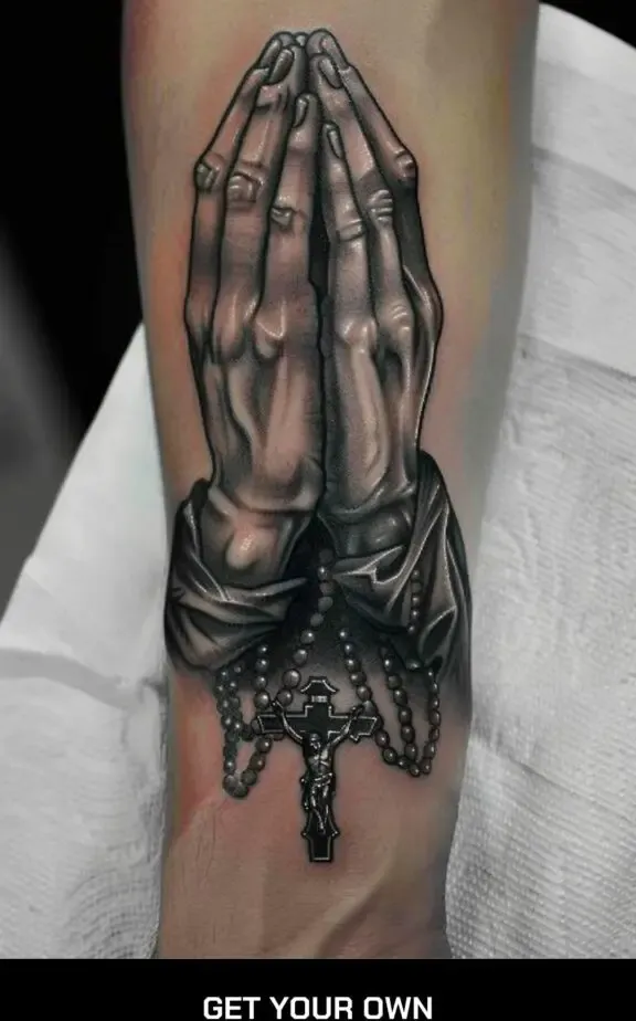 Praying hands tattoo with a rosary draped over them, symbolizing devotion.
